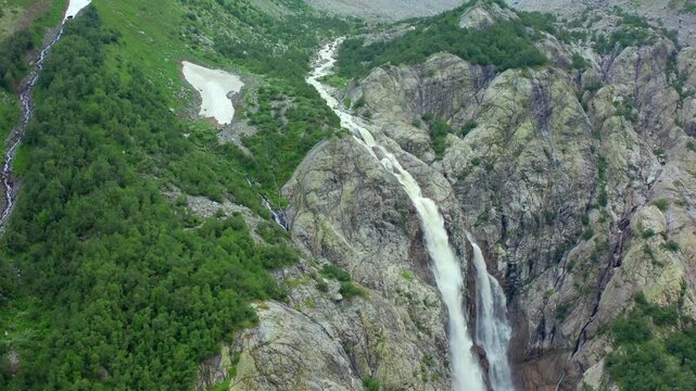 Shdugra Waterfall cascades in aerial view down a steep rock face below Ushba glaciers near Mazeri, Svaneti, supporting hiking tourism, glacial hydrology, geology research and Georgian travel promotion