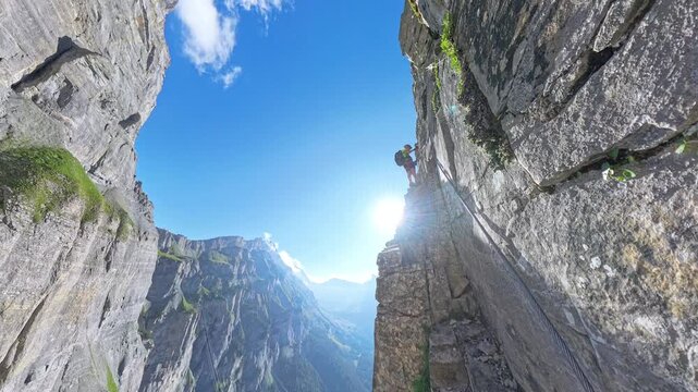 Climber ascending steep vertical rock face on Dauberhorn via ferrata, over background Gemmi Pass, Switzerland