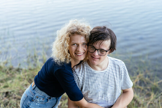 Caring Blonde Middle Aged Mother Hugging Teenage Son by Peaceful Mountain Lake in Spain