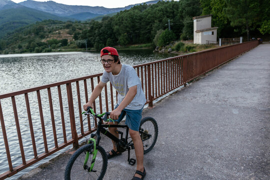 Full Length of Teenage Boy with Down Syndrome Riding Bicycle on Scenic Bridge