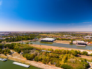 Fototapeta premium View of a river and cityscape during a clear day. A river flows through a city with buildings and green areas visible. The sky is clear and bright.