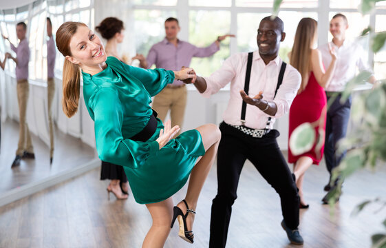 Group of happy men and women in festive clothes dancing foxtrot in dance studio
