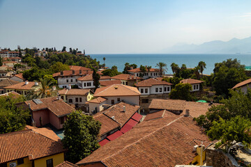 Fototapeta premium Classic panoramic view of Kaleici old town in Antalya, Turkey. Traditional white houses with red tiled roofs, Mediterranean sea coast, palm trees, and mountain horizon view.