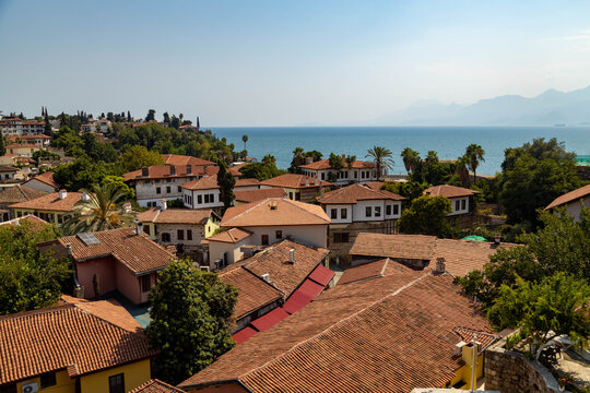 Classic panoramic view of Kaleici old town in Antalya, Turkey. Traditional white houses with red tiled roofs, Mediterranean sea coast, palm trees, and mountain horizon view.