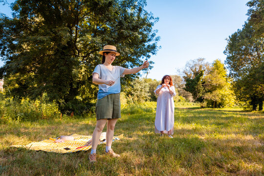 Adult daughter and mother spend time at a picnic in a bright summer park connecting with nature and enjoying joyful family leisure activities. Full length shot