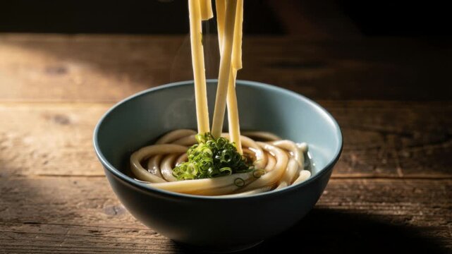 Steaming hot udon noodles served in a bowl with fresh green onions on rustic wooden table