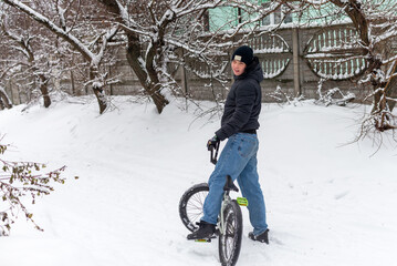 Naklejka premium Teenager boy riding a BMX bicycle in a snowy winter park or backyard