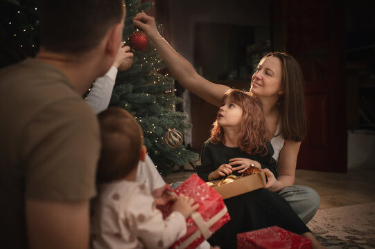 A large family of three children, mom and dad, are celebrating New Year's and Christmas under the Christmas tree at home, opening presents. A quiet, cozy family evening.