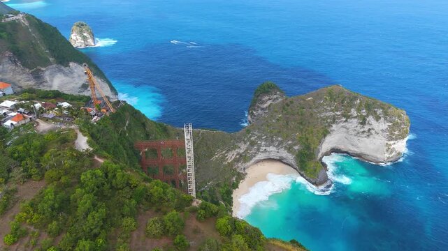 Controversial elevator structure construction at Kelingking Beach, Nusa Penida, Indonesia, with limestone landscape and turquoise ocean waters, aerial view