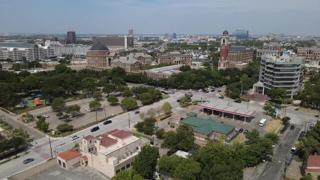 Clocktower landmark anchors busy Oak Lawn Avenue in Dallas. Extensive surface parking asphalt separates multi story corporate centers from retail gas station canopies, Texas