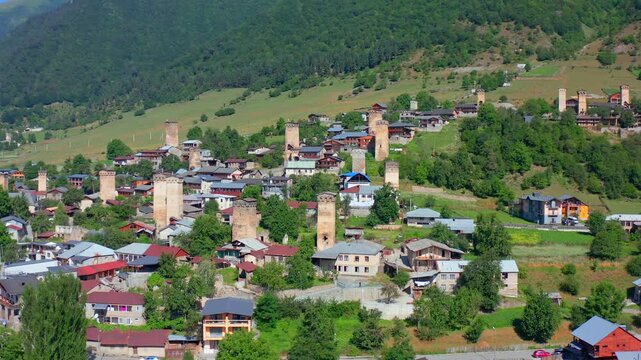 Mestia towers fill forward aerial view across traditional neighborhood, green slopes in Upper Svaneti, Georgia, supporting heritage tourism, medieval history, architecture, Caucasus destination media