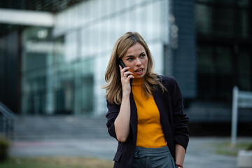 Fototapeta premium Businesswoman talking on smartphone outside office building