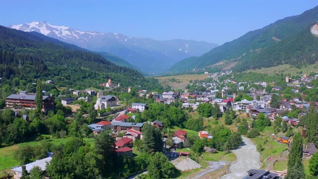 Mestia town expands in forward aerial view beneath Caucasus ridges and historic Svan towers, supporting Georgian tourism, mountain settlement geography, heritage travel, regional destination promotion