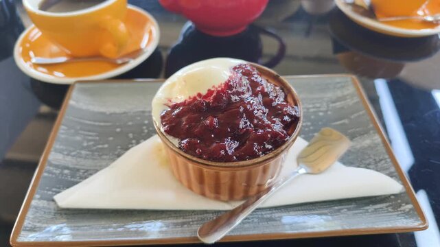 Delicious sweet dessert in ceramic ramekin served with jam and ice cream on plate. Tasty sweet dessert placed on table with teapot and colorful cups in cafe during cozy tea time service.