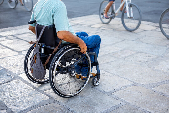 Wheelchair User Crossing Stone Plaza with Cyclists. Rear view of a person using a manual wheelchair on a stone plaza while cyclists pass in the background.