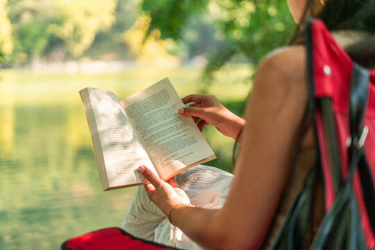 Woman reading book by lake on summer day