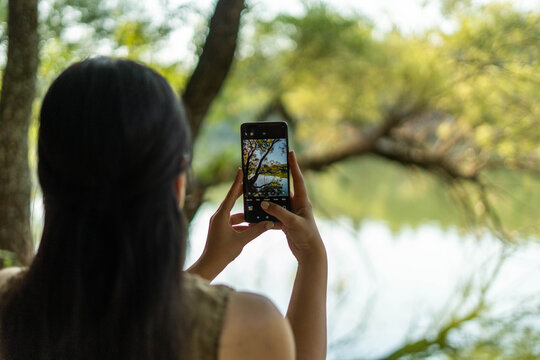 Woman capturing nature landscape with smartphone by lake