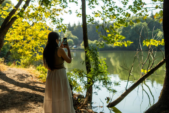 Woman wearing face mask photographing lake nature with smartphone