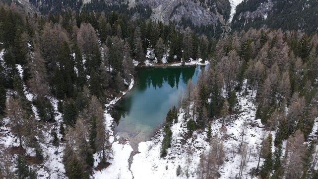 Alpine lake surrounded by evergreen pine forest and snow covered mountain slope in Maloja Pass, Switzerland. Aerial backward
