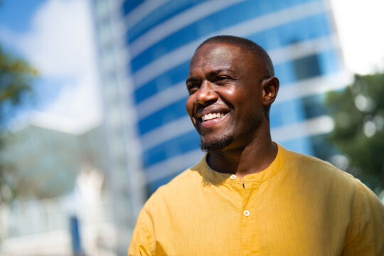 Black smiling businessman, closeup headshot face portrait, near glass office building. Young African american business man works as Banker, confident expression, meeting customer, career focused.