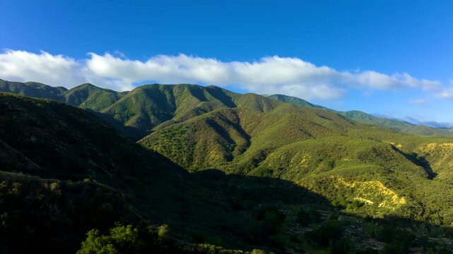 Aerial drone footage of rolling green mountains under blue sky with clouds in southern california landscape.