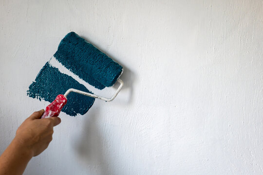 Hand Applying Teal Paint to a Textured White Wall with Roller
