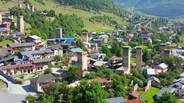 Svan towers fill elevated aerial view as drone circles Mestia neighborhoods beneath Caucasus slopes, supporting cultural tourism, medieval history, architectural preservation, Georgian travel media