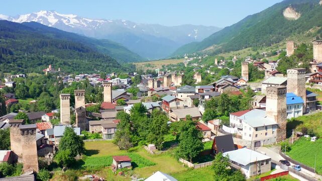 Mestia settlement fills elevated aerial view as the drone circles medieval Svan towers, village roofs and mountain slopes, supporting heritage tourism, cultural geography and architecture research.