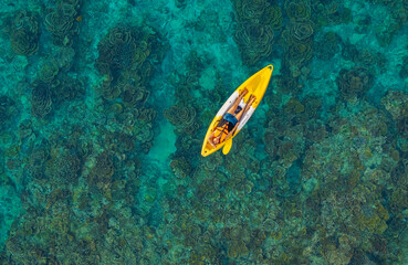 Aerial top view of a woman relaxing on a yellow kayak over a beautiful coral reef in crystal clear turquoise sea water. © SASITHORN