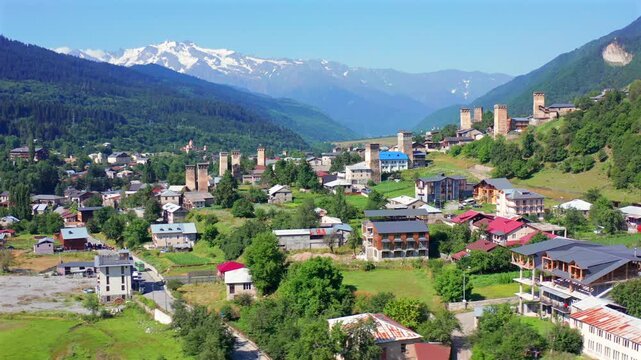 Mestia towers fill elevated aerial view as drone circles village homes, green fields and Caucasus foothills, supporting cultural tourism, medieval architecture, regional geography,: heritage promotion
