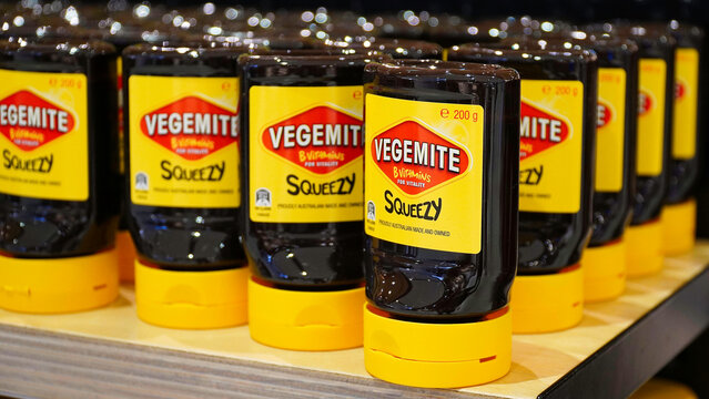 Squeezable Vegemite bottles displayed on a grocery store shelf during busy shopping hours