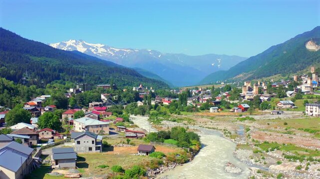 Enguri River fills forward aerial view beside Mestia homes and Caucasus slopes, supporting river geography, mountain tourism, settlement mapping, regional planning and Georgian destination promotion.