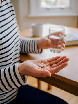 Close-Up of Man Holding Two Pill Capsules with Glass of Water