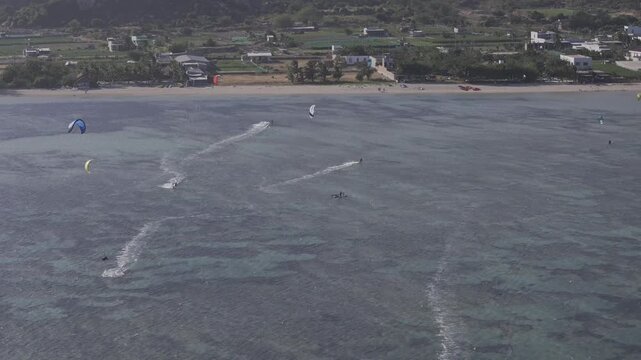 Aerial drone view of kite surfers riding the waves at My Hoa Beach in Vinh Hai, Khanh Hoa, Vietnam, showcasing a spectacular coastal landscape under bright sunlight.
