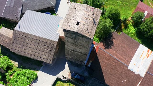 Svan tower fills circling aerial view above a traditional Mestia house and green garden, supporting medieval architecture, heritage conservation, cultural tourism and Georgian history media.