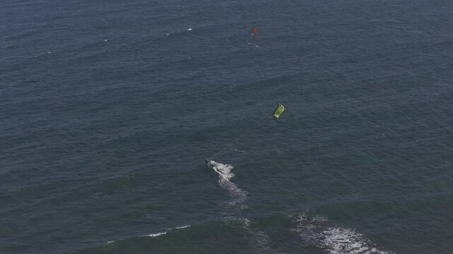 Aerial drone view of kite surfers riding the waves at My Hoa Beach in Vinh Hai, Khanh Hoa, Vietnam, showcasing a spectacular coastal landscape under bright sunlight.
