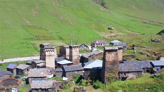 Ushguli tower houses pass in circling aerial view across green highland slopes, supporting vernacular architecture, medieval heritage, rural tourism and preservation media for Upper Svaneti, Georgia.