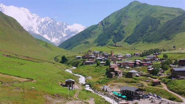 Chazhashi village approaches forward aerial view along the Enguri valley beneath Shkhara, supporting Upper Svaneti tourism, historic settlement geography, trekking routes, Georgian destination media