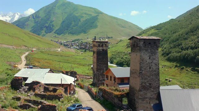 Drone advances past Svan towers in aerial view beside narrow Ushguli lanes and traditional homes, supporting defensive architecture, medieval history, heritage tourism, Georgian cultural documentaries