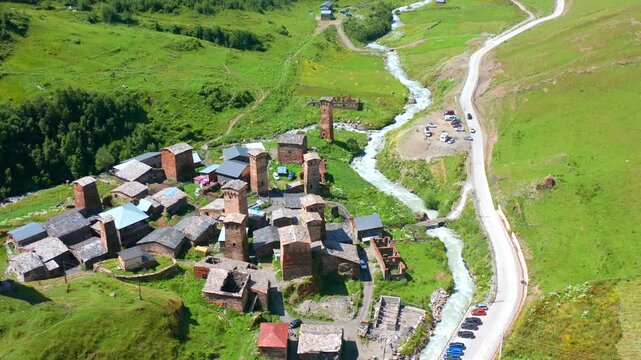 Chazhashi village approaches in forward aerial view above Svan towers, the Enguri River and mountain roads, supporting UNESCO heritage tourism, settlement mapping and Upper Svaneti travel promotion.