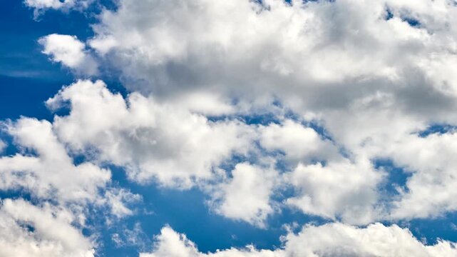Fluffy white cumulus clouds moving smoothly across a vibrant blue sunny sky on a clear summer day.