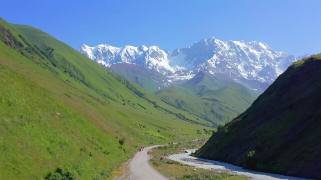 Mountain road approaches in forward aerial view along the Enguri valley toward Shkhara near Ushguli, supporting trekking access, scenic driving, route planning and Upper Svaneti destination promotion.