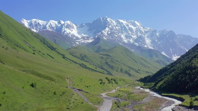 Drone flies forward above Shkhara valley along a remote alpine road near Ushguli, Upper Svaneti, supporting trekking tourism, expedition routes, mountain geography and Georgian destination promotion.