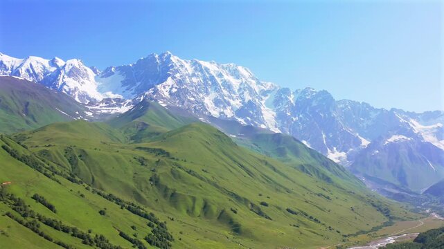 Drone circles Shkhara massif in aerial view above green alpine slopes, the Enguri valley near Ushguli, supporting mountain tourism, trekking campaigns, landscape geography, Georgian travel promotion