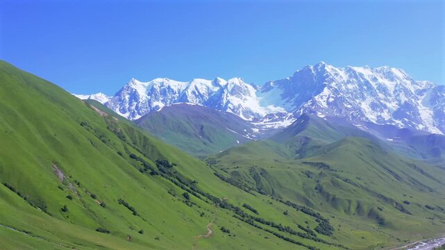 Drone circles Shkhara massif in aerial view above rolling alpine slopes and the Enguri valley near Ushguli, supporting hiking tourism, mountain geography, documentaries, Georgian destination marketing