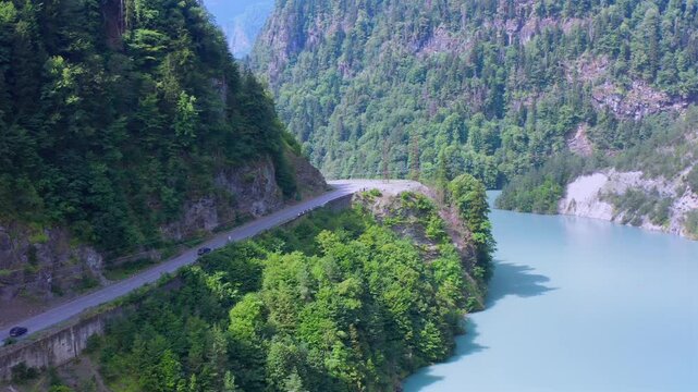 Drone hovers above Enguri Reservoir where a narrow road follows the forested shoreline through steep terrain, supporting regional tourism, transport planning, geography and infrastructure media.