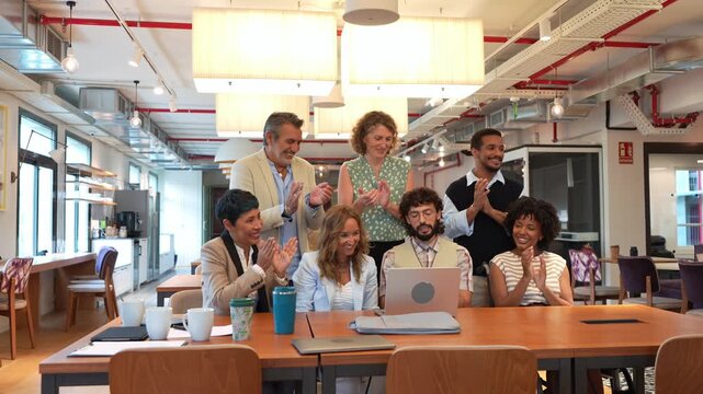 Diverse group of multiethnic coworkers celebrating a success in a meeting. Team applauding a colleague's work looking at a laptop computer