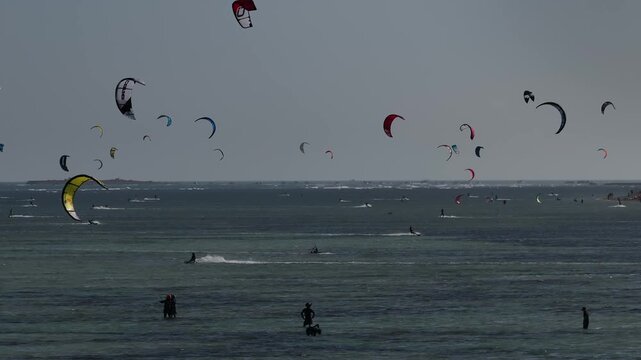 Aerial drone view of kite surfers riding the waves at My Hoa Beach in Vinh Hai, Khanh Hoa, Vietnam, showcasing a spectacular coastal landscape under bright sunlight.
