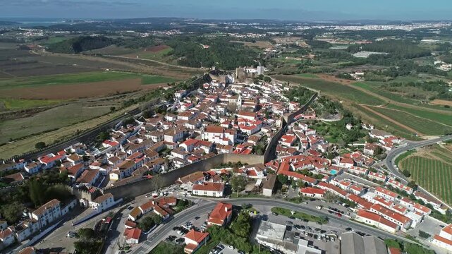Aerial view of the historic walled town of Obidos with its traditional white houses and terracotta rooftops surrounded by green fields and vineyards in Obidos, Leiria District, Portugal.