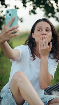 Portrait of a cheerful young woman taking a selfie with a smartphone, smiling and enjoying a fun moment, capturing modern lifestyle, social media and positive emotions.